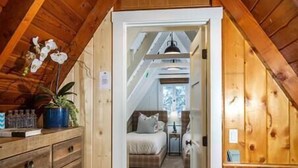 Un estrecho pasillo de madera que conduce a un dormitorio con cama y mesita de noche.