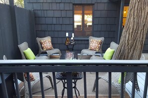 An outdoor patio with wicker furniture and a table, a window with a view, and a tree trunk to the right.