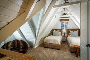 A cozy attic bedroom with a sloped ceiling, two beds, a chair, and a desk.