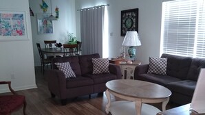 Ein Wohnzimmer mit einer braunen Couch, einem runden Couchtisch und einem Essbereich mit Tisch und Stühlen.
