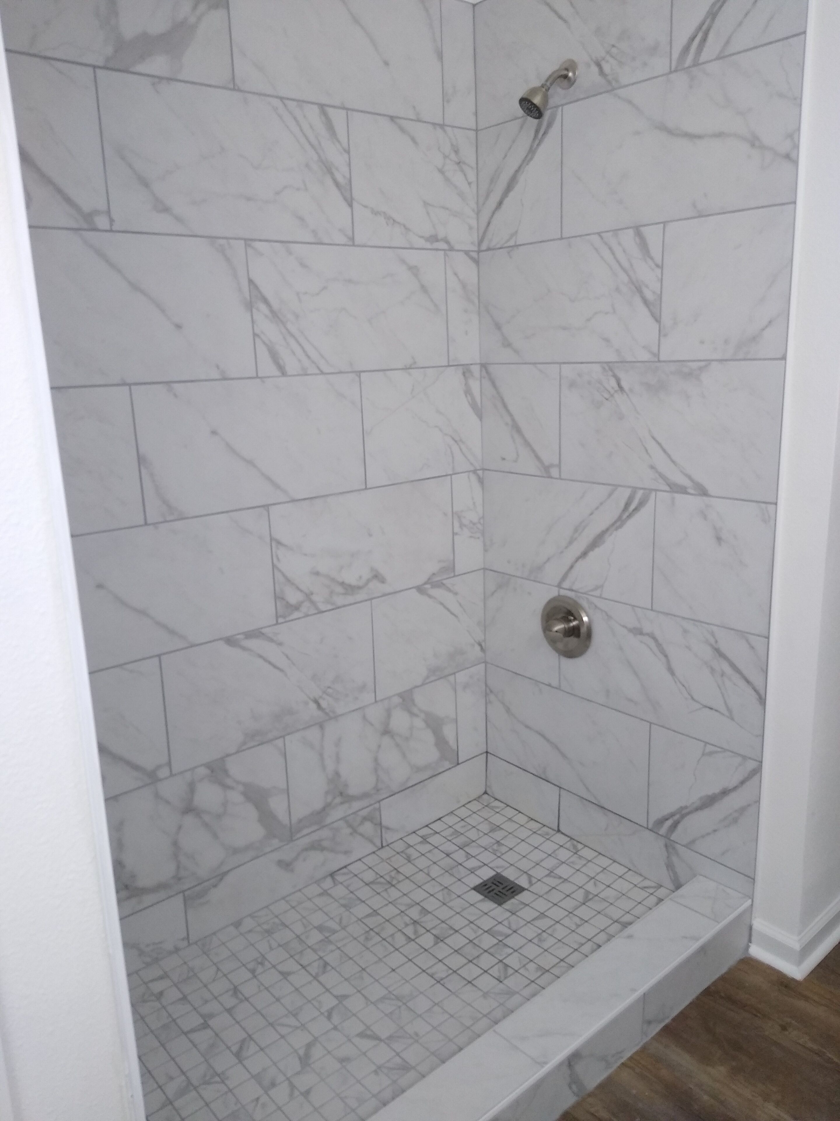 A shower with white marble tiles and a grid drain.
