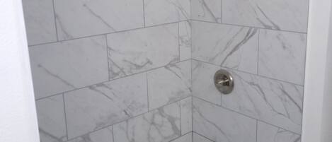 A shower with white marble tiles and a grid drain.