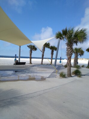 Een pad langs het strand met palmbomen, een bankje en een schaduwrijk gebied.