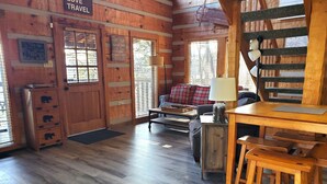A cozy log cabin interior with a wooden dining table, a sofa, and a staircase.