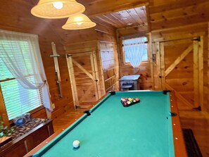A pool table in a wooden room with a window and curtains.