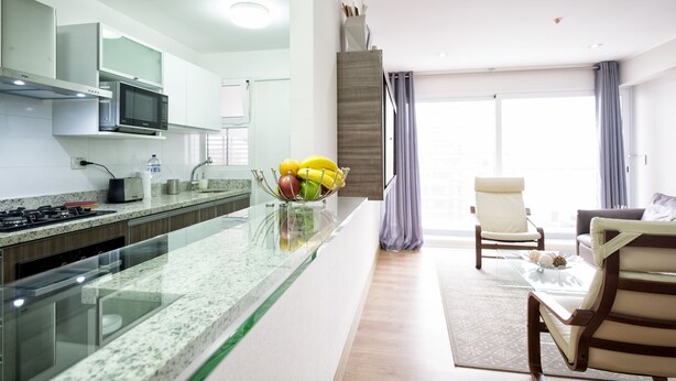 Een moderne keuken met een glazen eiland, een magnetron en een gasfornuis. Er is een eetgedeelte met een glazen tafel en stoelen, en een uitzicht op de omgeving door grote ramen.