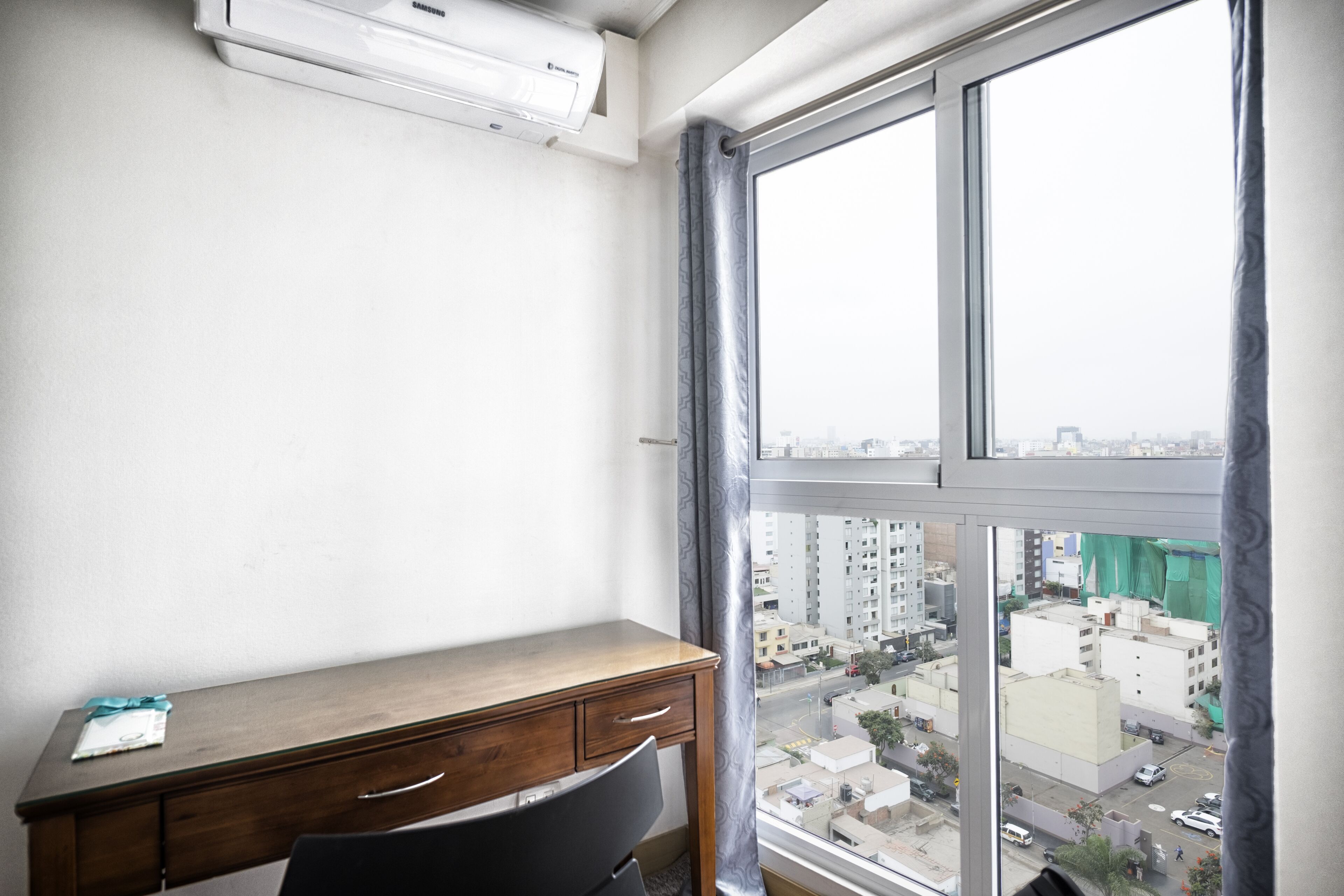 A room with a desk, a chair, and a large window with a view of a cityscape.