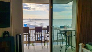 Habitación con vista a la playa, un balcón con sillas, una mesa y un televisor en la pared.