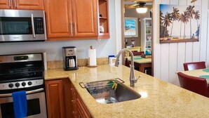 Una cocina con armarios de madera, un microondas de acero inoxidable, una cafetera y un lavabo con escurreplatos.