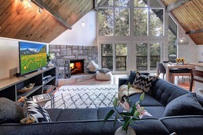A cozy living room with a stone fireplace, a large TV, and a comfortable seating area. - A-Frame Cabin | Game Room, Fire Pit, Sleeps 10 🌲 (Lake Arrowhead)