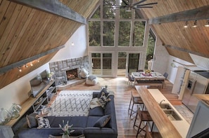 An interior with a stone fireplace, a dining area, and a kitchen with a wooden ceiling.
