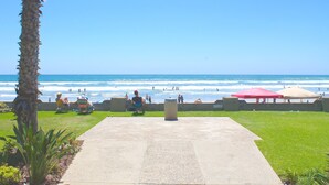 Une vue sur la plage avec une promenade en béton, des palmiers et des parasols de plage.