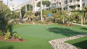 Un parcours de golf avec un green d’entraînement, entouré de palmiers et avec un ensemble de bâtiments en arrière-plan.