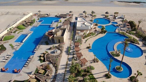 Un resort con varias piscinas, acceso a la playa y palmeras.