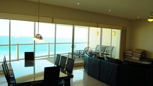 Una habitación amplia con una gran mesa de vidrio y sillas, un sofá y vista al océano.