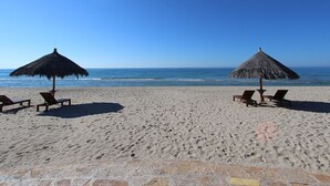 Una playa con dos sombrillas de paja y sillas de madera orientadas al océano.