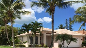 A house with a well-maintained lawn, palm trees, and a clear blue sky. - Naples Luxury Spotless 4 Bdrm Heated Pool Walk Bike To Beach  (Naples)