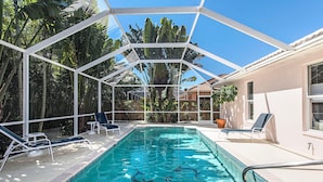 A swimming pool with clear blue water, surrounded by lounge chairs and a covered area with a white frame. - Naples Luxury Spotless 4 Bdrm Heated Pool Walk Bike To Beach  (Naples)