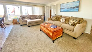 Een woonkamer met een beige bank, een houten salontafel en een schilderij van een haven.