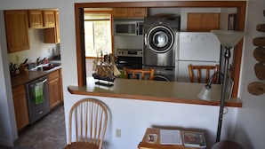 A compact kitchen with wooden cabinets, a microwave, a washing machine, and a refrigerator. - 1 Block From The Beach! (Seward)