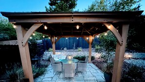An outdoor patio with a pergola, stone flooring, and a table with chairs. - Emerald House - striking, remodel in tranquil, central neighborhood (Redding)