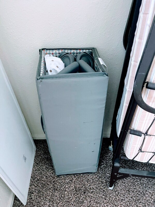A compact, gray laundry basket with a patterned top, placed against a wall with a textured surface.
