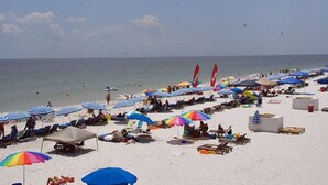 A beach with rows of sunbeds and umbrellas, a clear sky, and the ocean in the background.