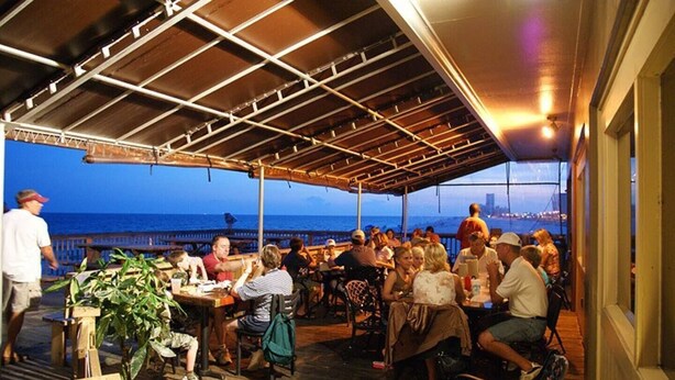 An outdoor dining area with tables and chairs, overlooking a body of water.