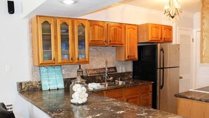 A kitchen with wooden cabinets, a granite countertop, a refrigerator, and a chandelier.