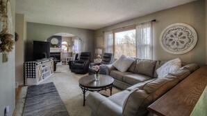 A living room with a sofa, armchairs, a coffee table, and a TV. There is a fireplace, a window with curtains, and a decorative wall piece. - Downtown Custer &  neighbor to Rock Crest Lodge (Custer)
