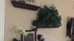 Un mur avec trois étagères en bois. L’étagère du haut porte une pancarte sur laquelle est écrit : « Croyez en vous et vous y parviendrez. » L’étagère du milieu contient une grande plante verte. L’étagère du bas présente une citation encadrée, une petite plante en pot et un objet décoratif.