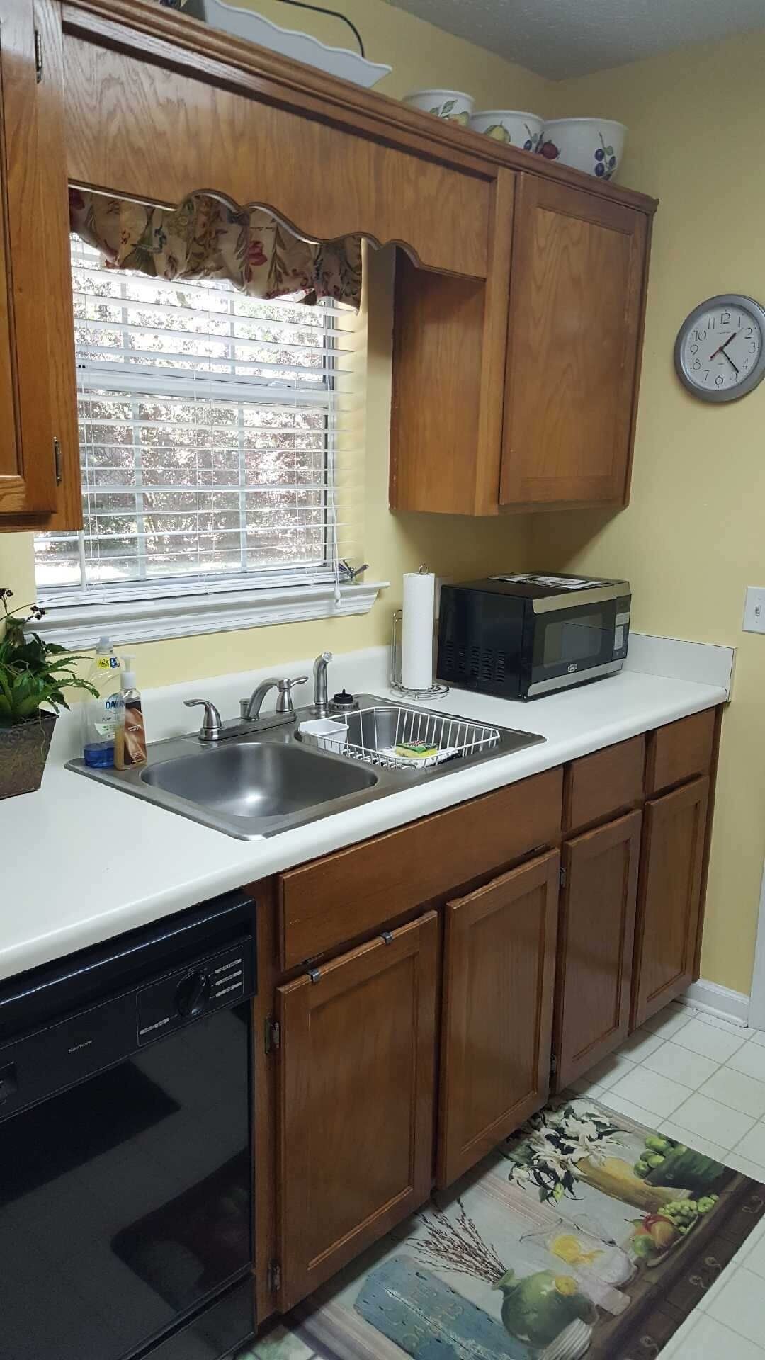 A kitchen with wooden cabinets, a dishwasher, a microwave, and a window with blinds.