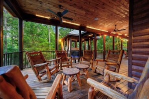 A wooden deck with rocking chairs and a small table, surrounded by a wooden cabin with a covered porch and a view of the forest. - Call It A Day- Pickleball Sport Court! Pool Table, Game Room (Broken Bow)