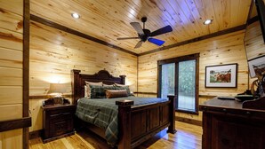 A wooden cabin bedroom with a bed, nightstands, a dresser, a ceiling fan, and a window with blinds.
