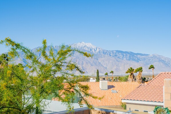 A residential area with a mountain in the background, houses with red-tiled roofs, and some palm trees.