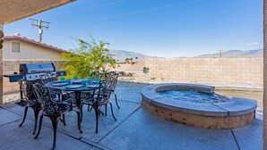 Un patio exterior con una parrilla, una mesa de comedor, sillas y un jacuzzi.