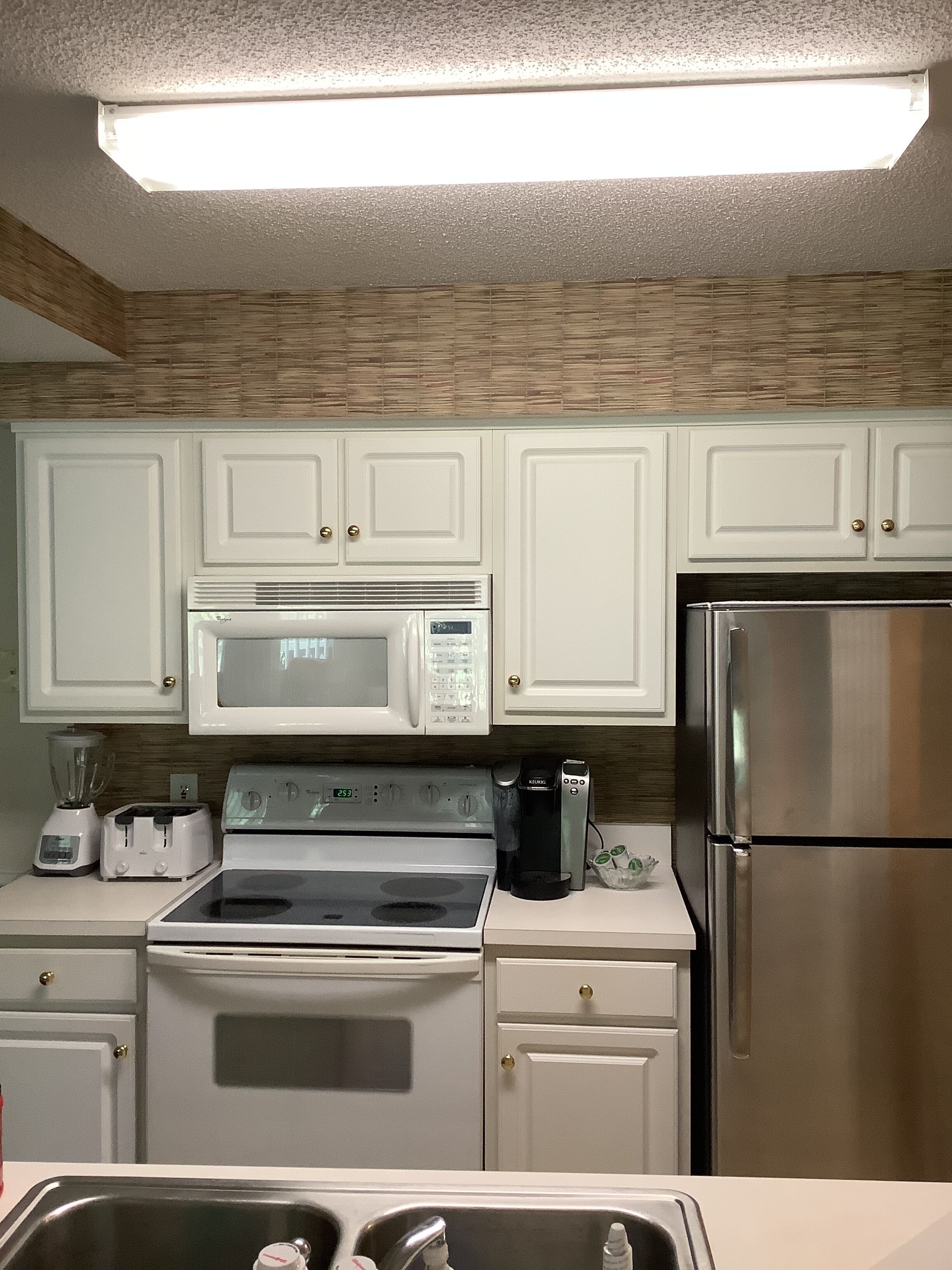 A kitchen with white cabinets, a stainless steel refrigerator, a microwave, a stove, and a coffee maker.
