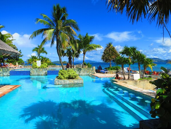 Ein Poolbereich mit Liegestühlen, Palmen und Blick auf das Meer.