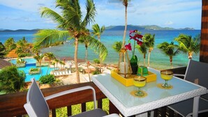 A terrace with a table set for two, overlooking a pool and a beach with palm trees and a clear view of the ocean. - ★★★★★ Beachfront Newly Renovated Penthouse Washer/Dryer Perfect for Family WiFi (St. Thomas)