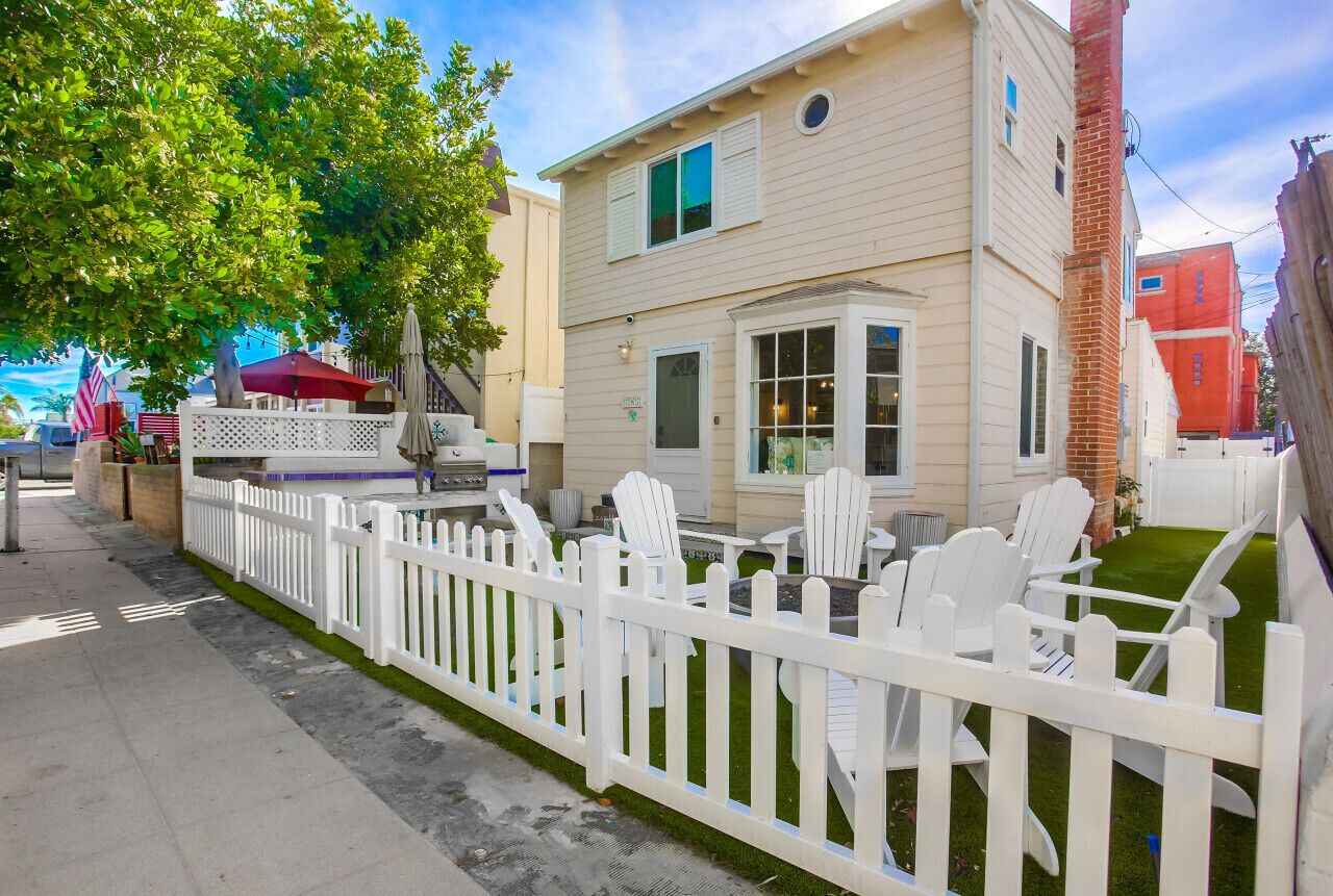 A two-story building with a white picket fence, outdoor seating with white chairs, and a small patio area.