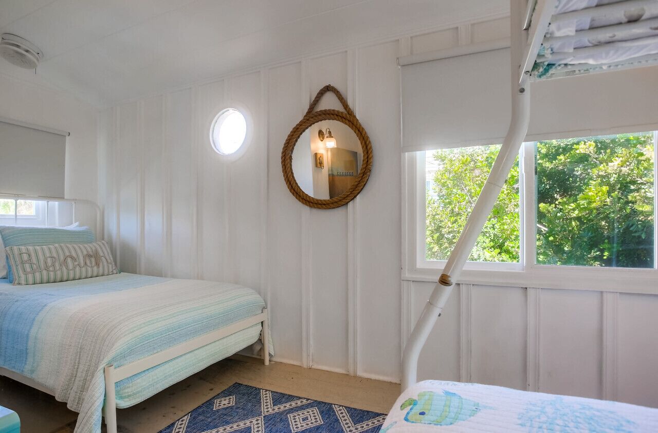 Una camera da letto con due letti, una finestra vista verde, uno specchio tondo e una lampada a soffitto.