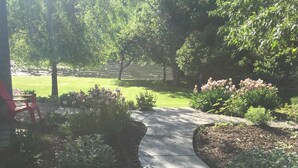 A curved concrete pathway in a landscaped garden area with various plants and shrubs. - Missouri Riverfront Bungalow Near Craig MT. (Cascade)