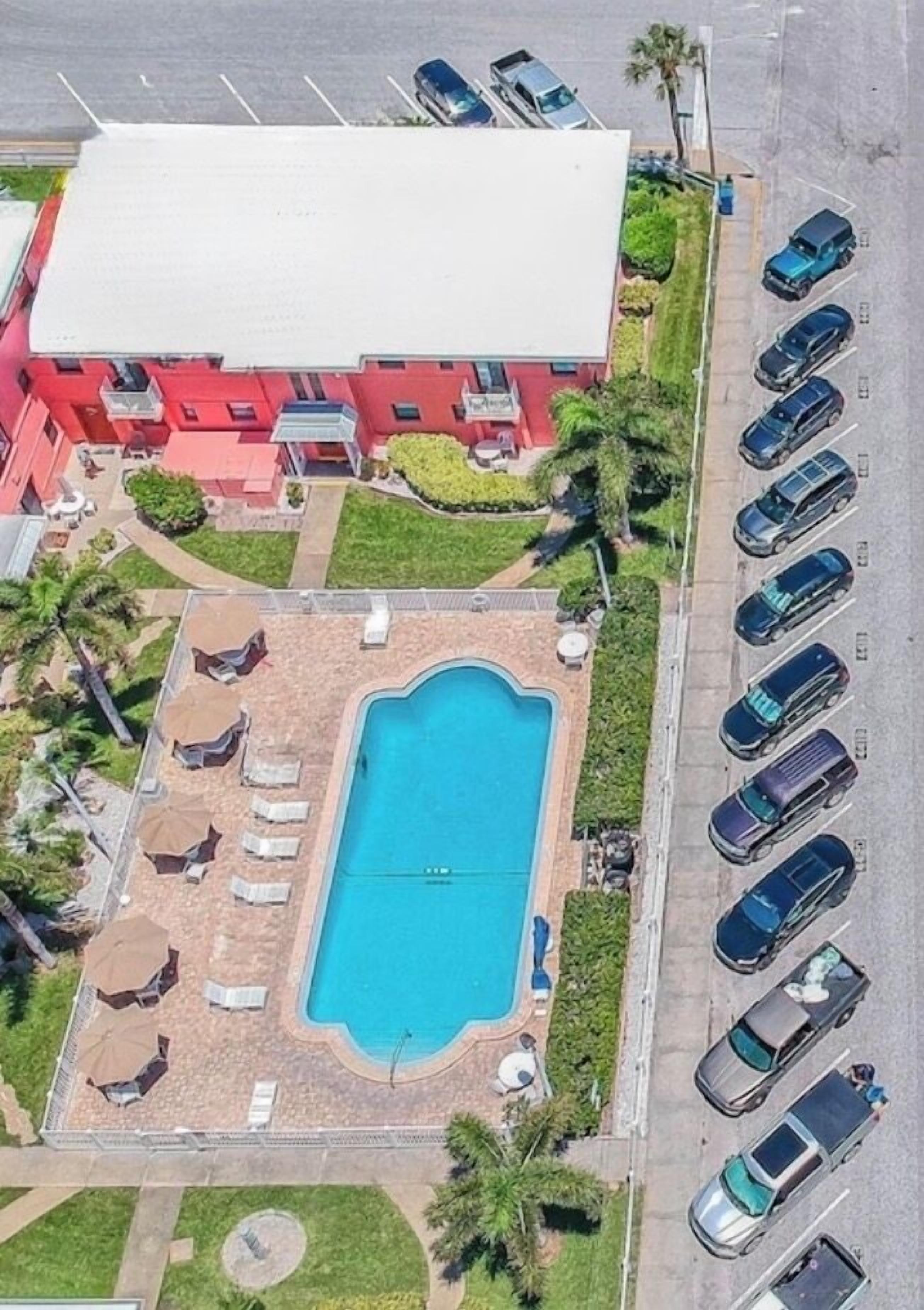 Vista aérea de um hotel com piscina, estacionamento e um edifício vermelho com várias sacadas.