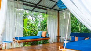 A wooden deck with a hanging swing and a bed with blue bedding.
