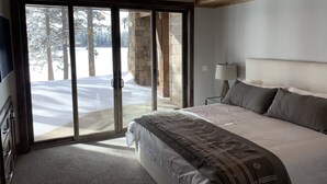 A bedroom with a large bed, a ceiling fan, a nightstand, and a view of a snowy landscape through the sliding glass doors.