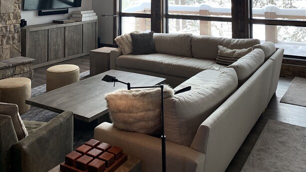 A spacious living room with a large sectional sofa, a flat-screen TV mounted on a stone wall, and a stone fireplace.