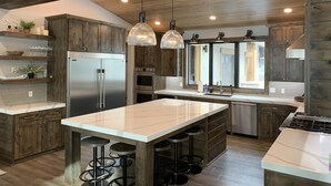 A modern kitchen with wooden cabinets, a stainless steel refrigerator, an oven, a sink, and a bar area with stools.