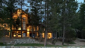 A large, multi-story log cabin with a stone foundation, surrounded by trees.