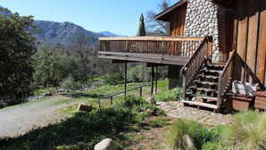 Une cabane rustique dotée d’une cheminée en pierre, d’une terrasse en bois et d’un escalier menant à un porche.
