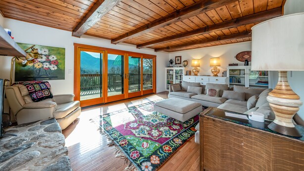 Un salon spacieux avec un plafond en bois, une grande fenêtre offrant une vue sur les montagnes, un canapé confortable, une table basse et un tapis coloré.